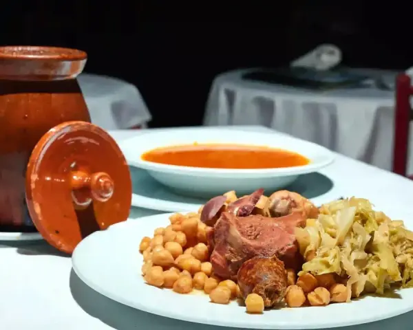 Plato de cocido madrileño con garbanzos, carne, repollo y sopa en un cuenco.