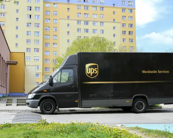 Czarny van UPS z napisem "Worldwide Services" na tle bloku mieszkalnego. Zastanawiasz się, ile zarabia kurier UPS?