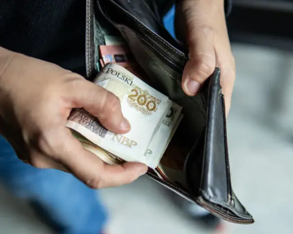Ręce wkładają polskie banknoty 200 zł do portfela. Czy można mieć dwóch komorników na pensji, gdy pieniędzy jest tak mało?