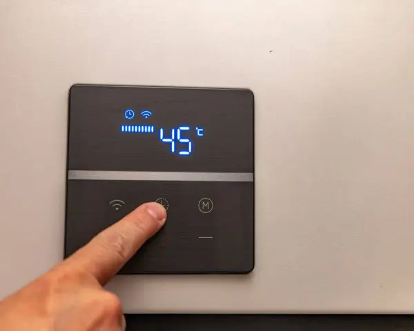 Dito, un dito preme il pulsante di un pannello digitale che mostra l'indicatore temperatura scaldabagno a 45°C, con icone Wi-Fi e di riscaldamento attive.