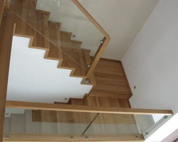 Nowoczesne schody dywanowe na beton, z drewnianymi stopniami i szklaną balustradą, tworzą lekkość i elegancję.