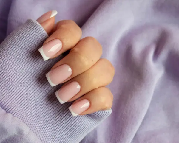 Dłoń z paznokciami w stylu french kolor, na tle lawendowej bluzy. Klasyka i elegancja.