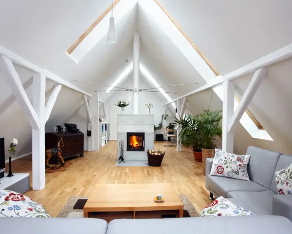 Aménagement comble 30m2 : salon cosy avec cheminée, canapé gris, parquet clair et poutres apparentes.