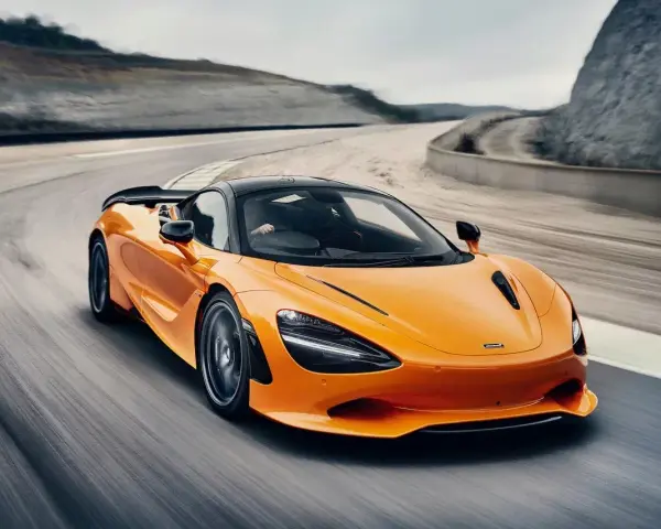 Pomarańczowy McLaren 750S z czarnym dachem sunie po torze wyścigowym, tworząc dynamiczny obraz prędkości i mocy.