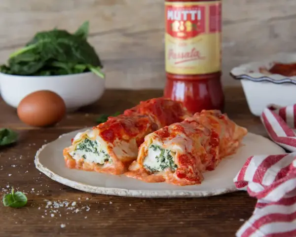 Cannelloni ricotta e spinaci fumanti, conditi con passata Mutti e formaggio filante, pronti per essere gustati.