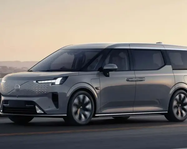 Szary luksusowy van elektryczny Volvo EM90 w ruchu drogowym nad morzem.