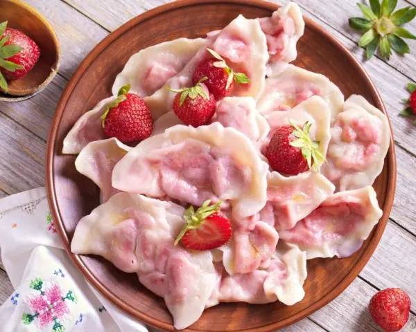 Pyszne pierogi z truskawkami, ozdobione świeżymi owocami, wyglądają apetycznie na glinianym talerzu.