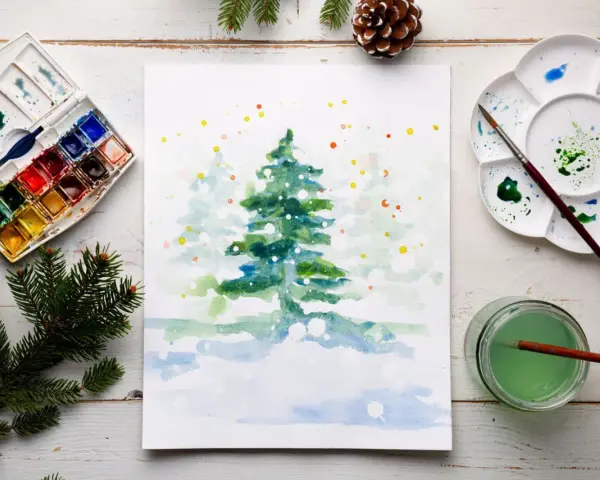 Pintura de acuarela de un árbol de Navidad nevado, con una paleta de acuarelas y pinceles, ideal para una acuarela navidad facil.