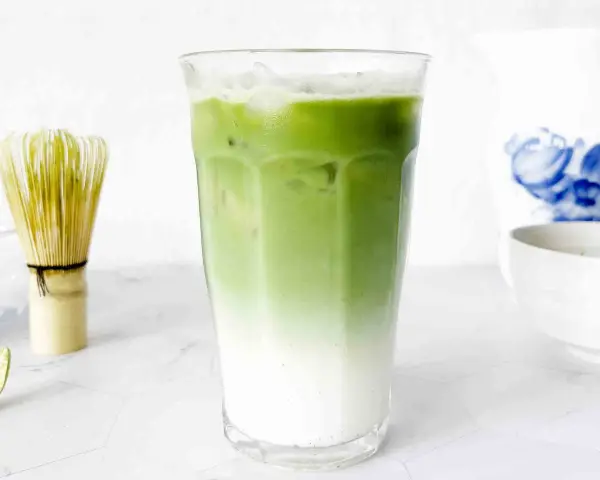 En isig matcha latte med lager av mjölk och grönt te. Bredvid står en bambuvisp, redo att blanda nästa goda dryck.