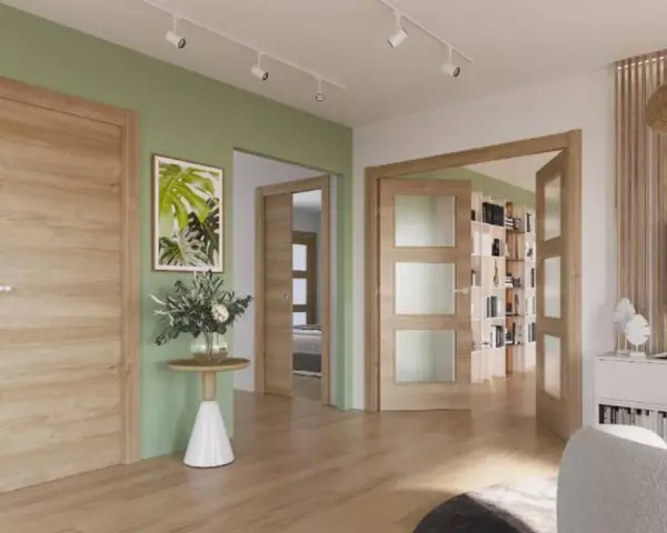 Un pasillo con paredes verde menta y puertas de roble. Un cuadro de hojas tropicales y un jarrón con flores adornan la pared.
