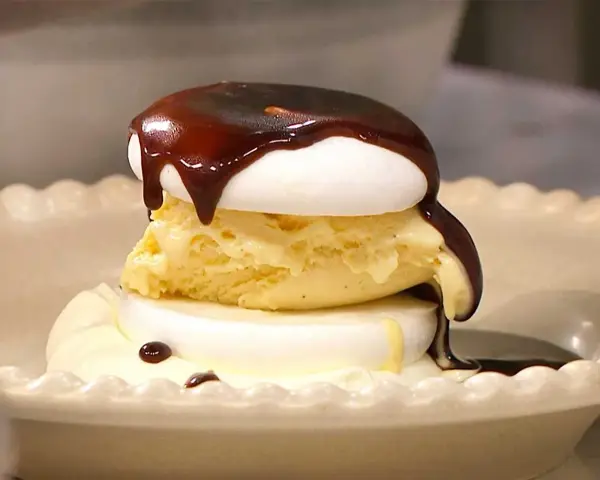 En läcker banana split med vaniljglass, maräng och chokladsås som rinner ner.