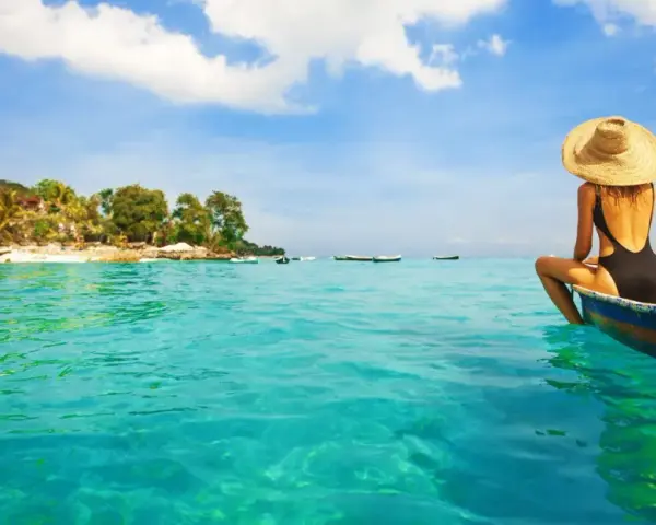 Kobieta w kapeluszu siedzi na łodzi, podziwiając turkusowe morze i tropikalne plaże na Bali.