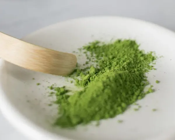 Zielony proszek matcha na białej miseczce, gotowy do przygotowania napoju. Poznaj, jak smakuje matcha – intensywnie, lekko gorzko, z nutą słodyczy.