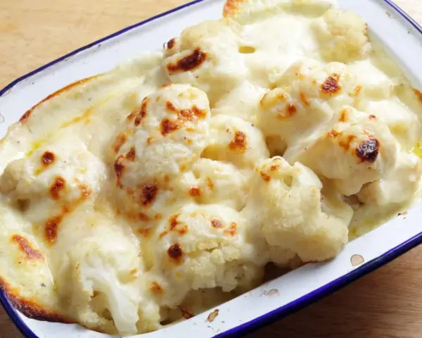 Coliflor gratinada con bechamel cremosa, dorada y burbujeante en una fuente.