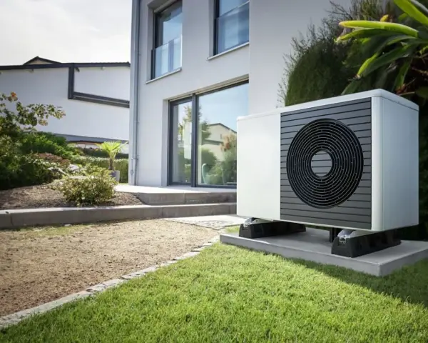 Un moderno sistema hvac, una unidad exterior blanca con rejilla circular negra, se asienta sobre una base de hormigón en un jardín cuidado.