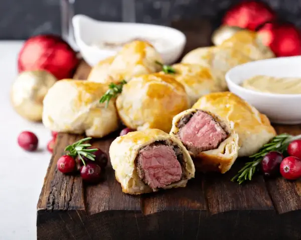 Bouchées à la reine dorées, garnies de viande juteuse, sur une planche en bois avec des canneberges et des décorations festives.