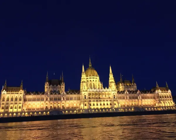 Budynek Parlamentu w Budapeszcie nocą, oświetlony, z odbiciem w Dunaju. Warto sprawdzić ceny na Węgrzech przed podróżą.