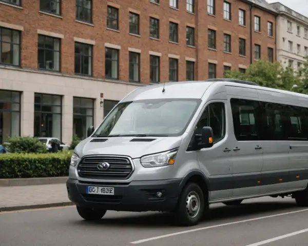 Un homme est au volant, prêt à conduire un minibus argenté dans une rue bordée d'arbres et de bâtiments.