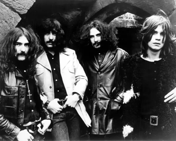 Czterech członków zespołu Black Sabbath, ikony heavy metalu, pozuje do zdjęcia. Ich mroczny styl zapowiadał przełomowe black sabbath albumy.