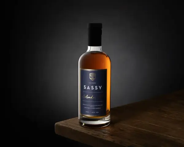 Packshot photo d'une bouteille de Calvados SASSY XO ambré, posée sur une table en bois.