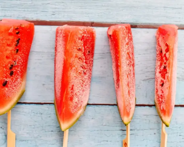 Vier gefrorene Wassermelonenstücke auf Stöcken, bereit zum Genießen. Eine erfrischende Idee für Wassermelone einfrieren.