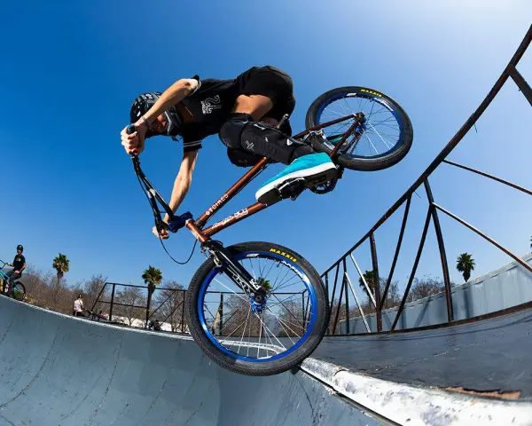 A BMX rider, possibly Chelsea Wolfe, performs a trick on a ramp against a clear blue sky.