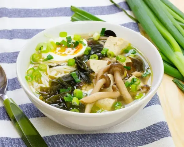 A miska pełna aromatycznej zupy miso z tofu, grzybami, wodorostami, jajkiem i szczypiorkiem.