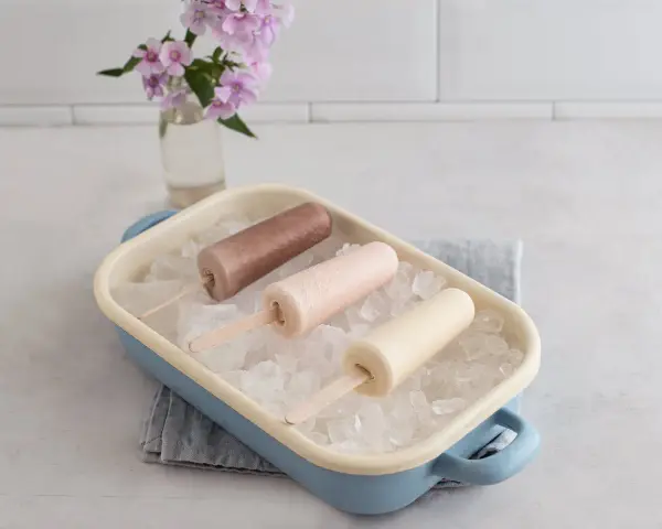Drei cremige Mini Milk Eis am Stiel, wie aus den 90ern, in einer blauen Schale auf Eiswürfeln.