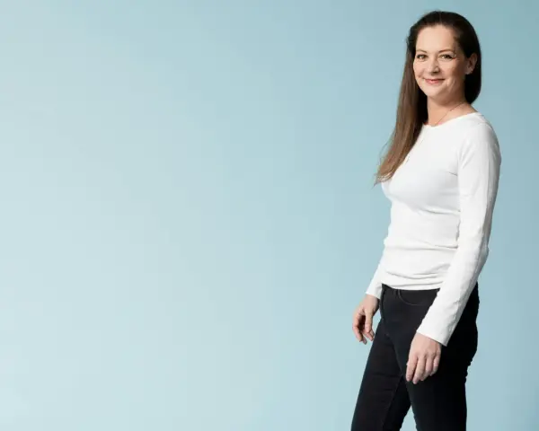 Kvinna i vit tröja och svarta jeans ler mot kameran, redo för en utmaning som fasta 24 timmar.