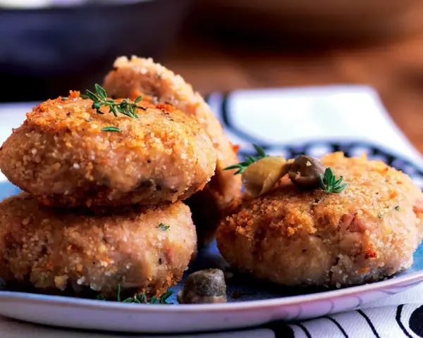 Polpette tonno e patate dorate e croccanti, guarnite con erbe aromatiche e olive, pronte per essere gustate.