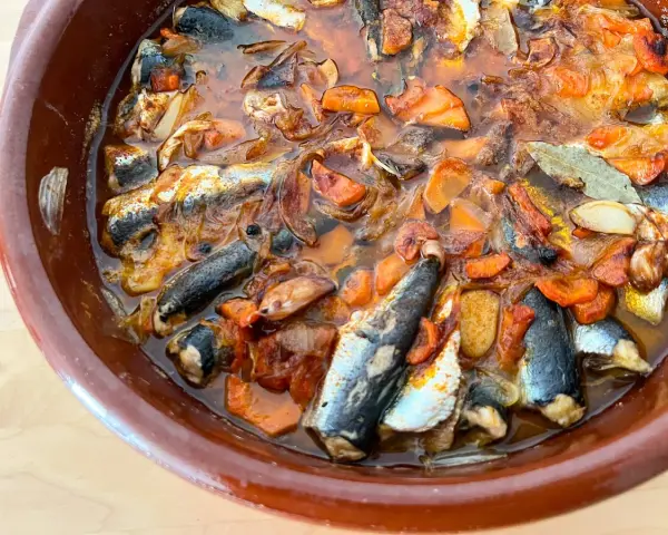 Sardinas en escabeche cocinándose en una cazuela de barro con verduras.