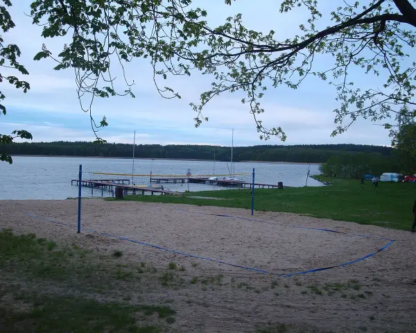Plaża z boiskiem do siatkówki plażowej nad jeziorem w Borneńskim Sulimowie. W tle pomosty, żaglówki i las.