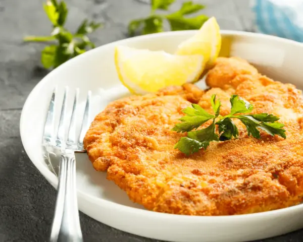 En gyllene schnitzel med citronklyfta och persilja, redo att avnjutas med ett glas vin till schnitzel.