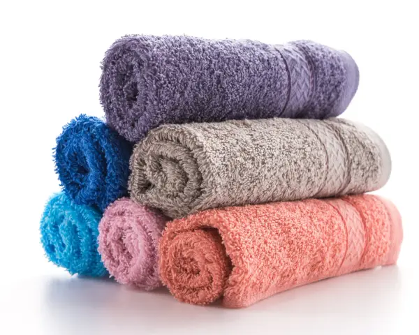 Pile de serviettes de bain roulées aux couleurs vives : violet, bleu, gris, rose et corail. La matière douce invite à la détente.