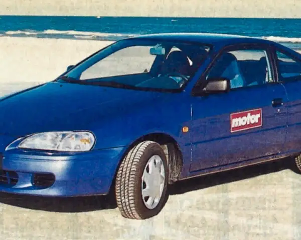 Niebieski Toyota Paseo stoi na plaży, z morzem w tle.