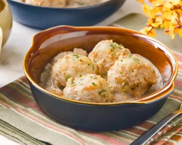 Cuatro albóndigas de merluza caseras en una cremosa salsa, espolvoreadas con perejil fresco.