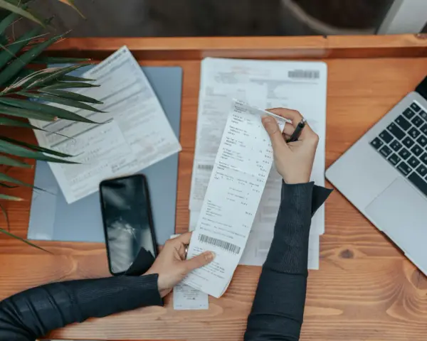 Osoba analizuje rachunki, laptop i telefon. Frankowicze nie muszą spłacać kredytu w trakcie procesu, co może być tematem analizy.