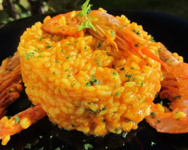 Arroz con gambones, un plato vibrante y delicioso, coronado con gambones jugosos y perejil fresco.