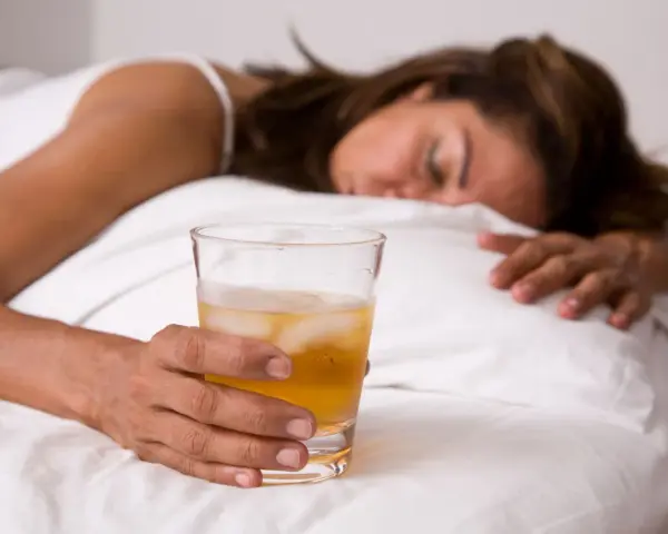 Kobieta w łóżku z drinkiem, nieświadoma. Objawy po zażyciu pigulka gwaltu mogą być różne.
