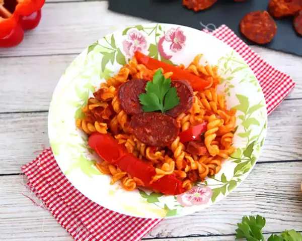 Pyszny makaron z chorizo, papryką i natką pietruszki na talerzu z motywem kwiatowym.