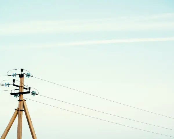Drewniany słup na działce, który stoi tam od ponad 30 lat, z przewodami elektrycznymi na tle jasnego nieba.