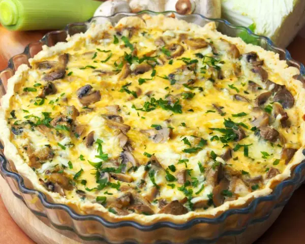 Pyszny quiche z pieczarkami, posypany świeżą natką pietruszki, w szklanej formie.