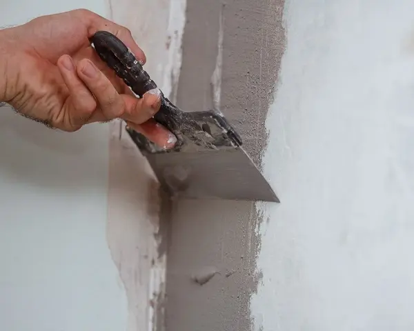 Mano che usa una spatola per stuccare un muro, creando una superficie liscia e uniforme per la pittura.