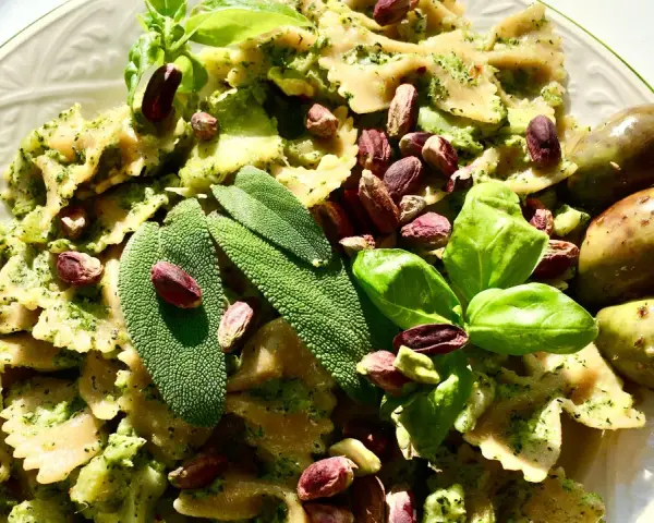 Farfalle condite con un saporito pesto di salvia, guarnite con pistacchi, basilico e olive.