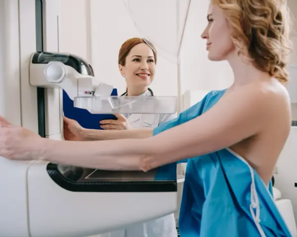 Kobieta przygotowuje się do mammografii, podczas gdy radiolog uśmiecha się wspierająco.