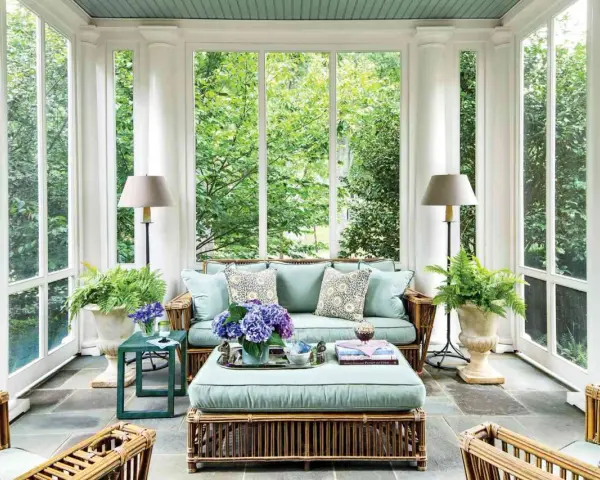 A serene screen porch with rattan furniture, plush cushions, and lush greenery. The natural screen porch materials create a cozy, inviting atmosphere.