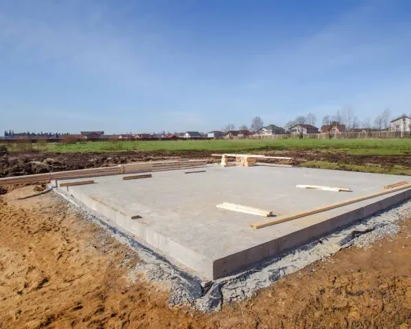 Betonowe ławy fundamentowe gotowe na nowy dom. W tle widać domy i zielone pola.