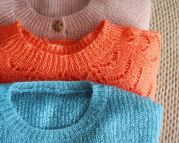 Gestapelte Pullover in Rosa, Orange und Blau. So kannst du deine **Wolle richtig waschen** und sie bleibt schön.