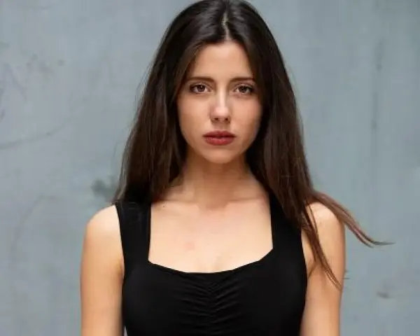 Ritratto di una giovane donna con lunghi capelli castani, indossa un abito nero. Il suo sguardo è intenso, come se stesse aspettando qualcuno, forse celeste dalla porta.