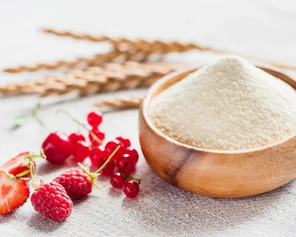 Miseczka z semoliną, obok świeże owoce: maliny, truskawki, porzeczki i kłosy zbóż. Semolina co to? To mąka z pszenicy durum.